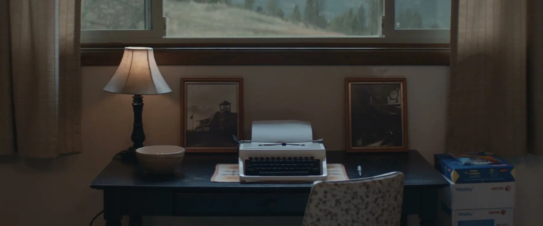 Typewriter, lamp and framed photographs beneath a window in Mabel