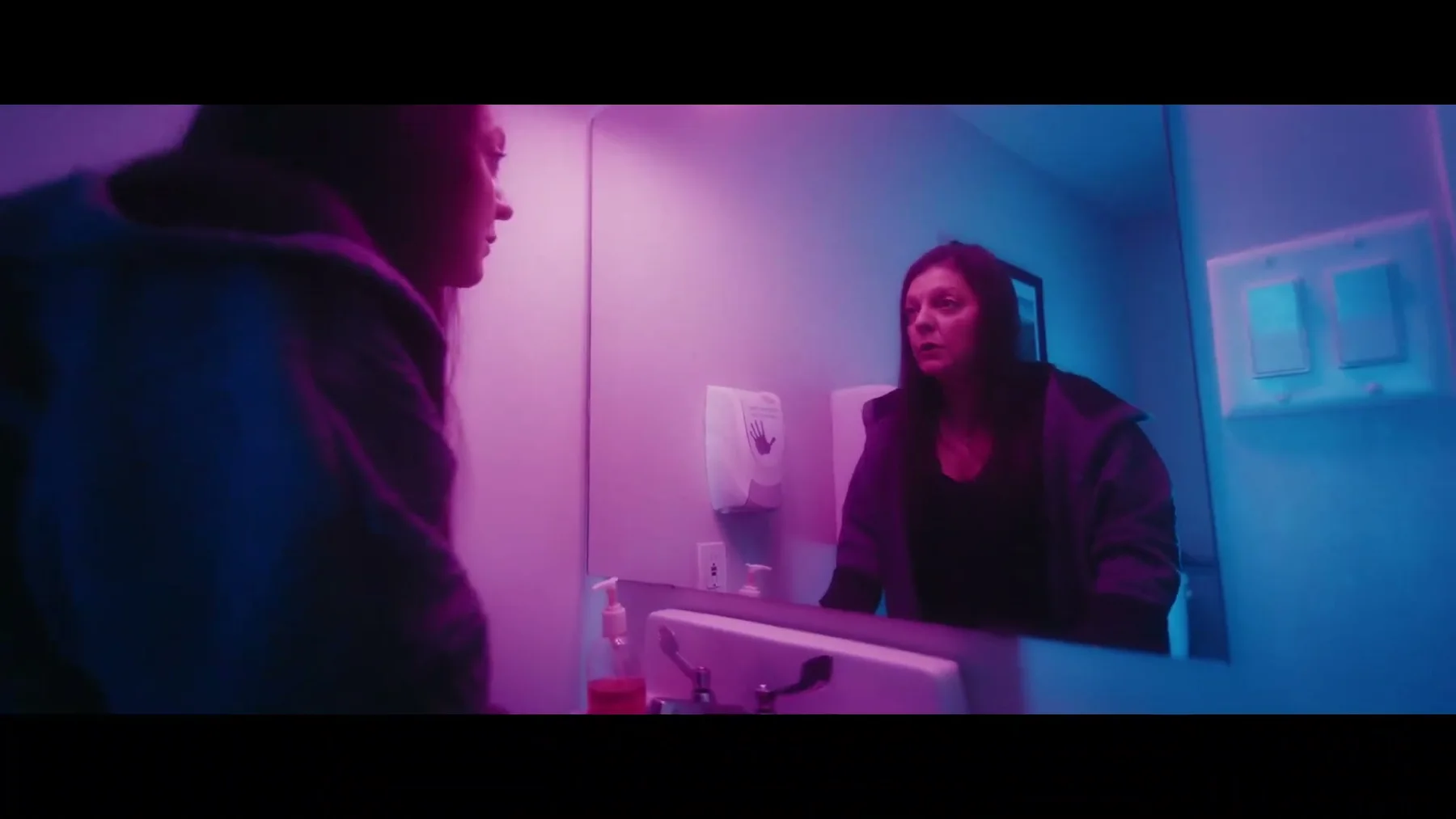 A participant facing her reflection under magenta and blue light in Midlife Shuffle