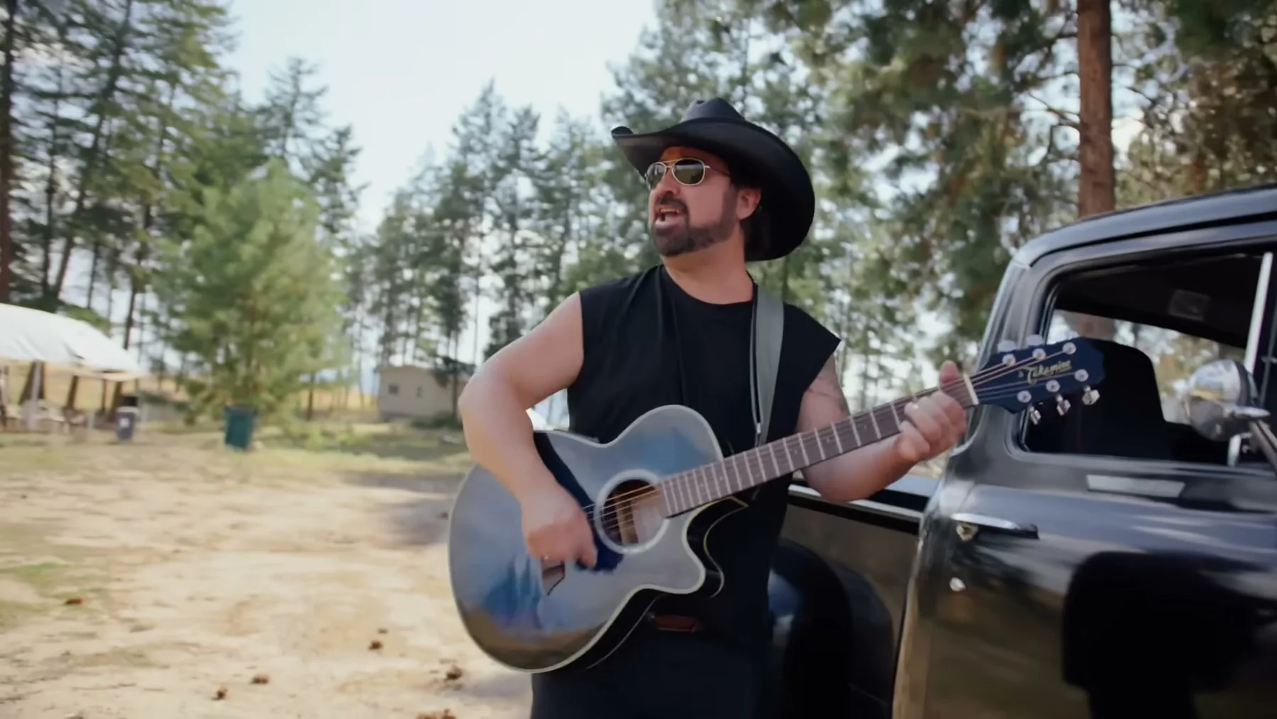 Kris Anders playing acoustic guitar beside a vintage pickup in Open Road