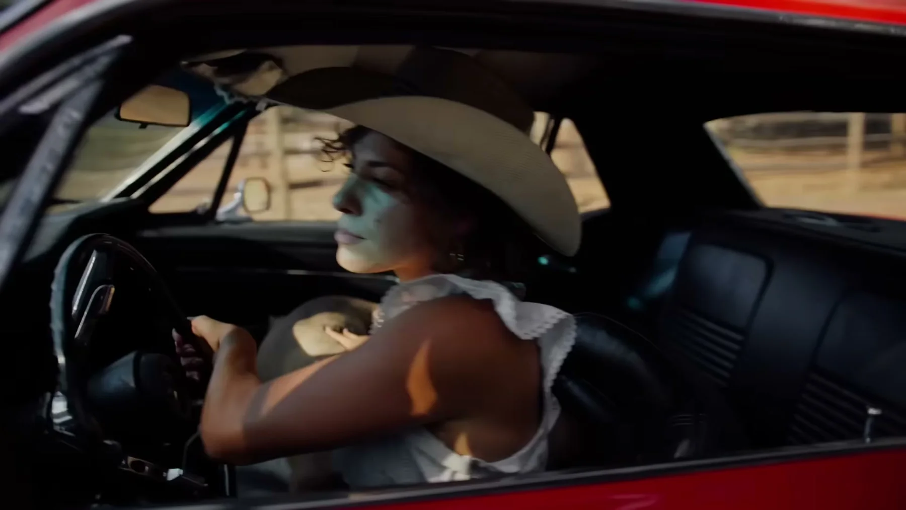 Driver in a white cowboy hat behind the wheel of a red convertible in Open Road