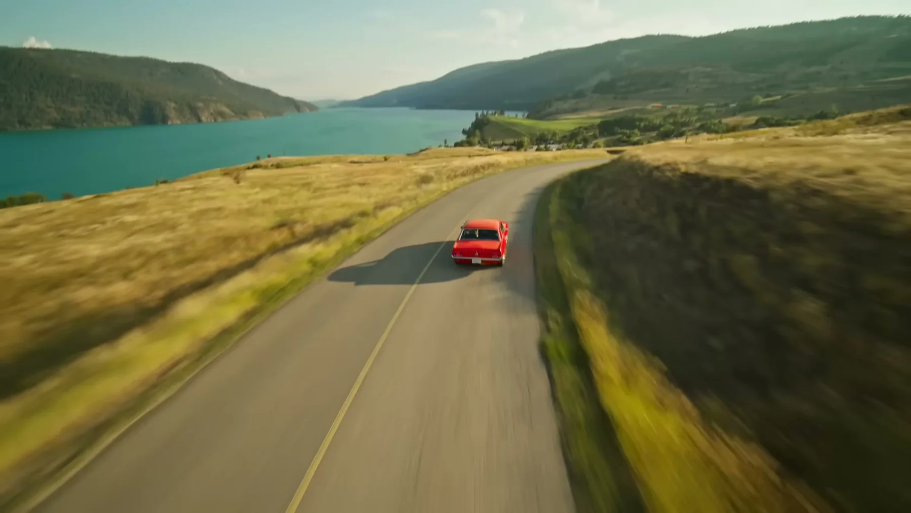 Red pickup travelling along a lakeside road in Open Road
